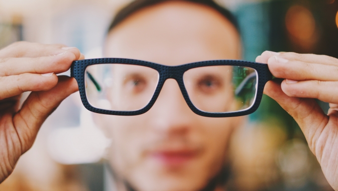 Photo d'un personne regardant l'objectif au travers d'une paire de lunettes tenue à distance.