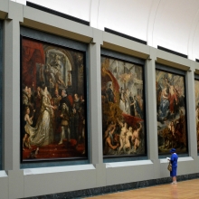 Une personne devant des tableaux dans une galerie du Musée du Louvre.